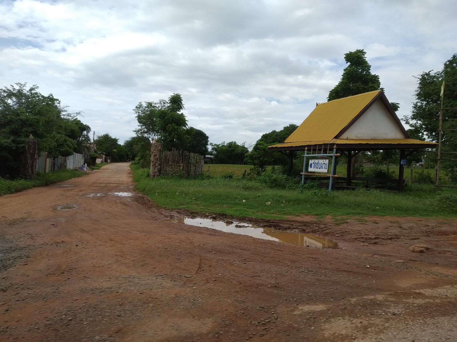 Red dirt road past a village temple shelter in rural Thailand